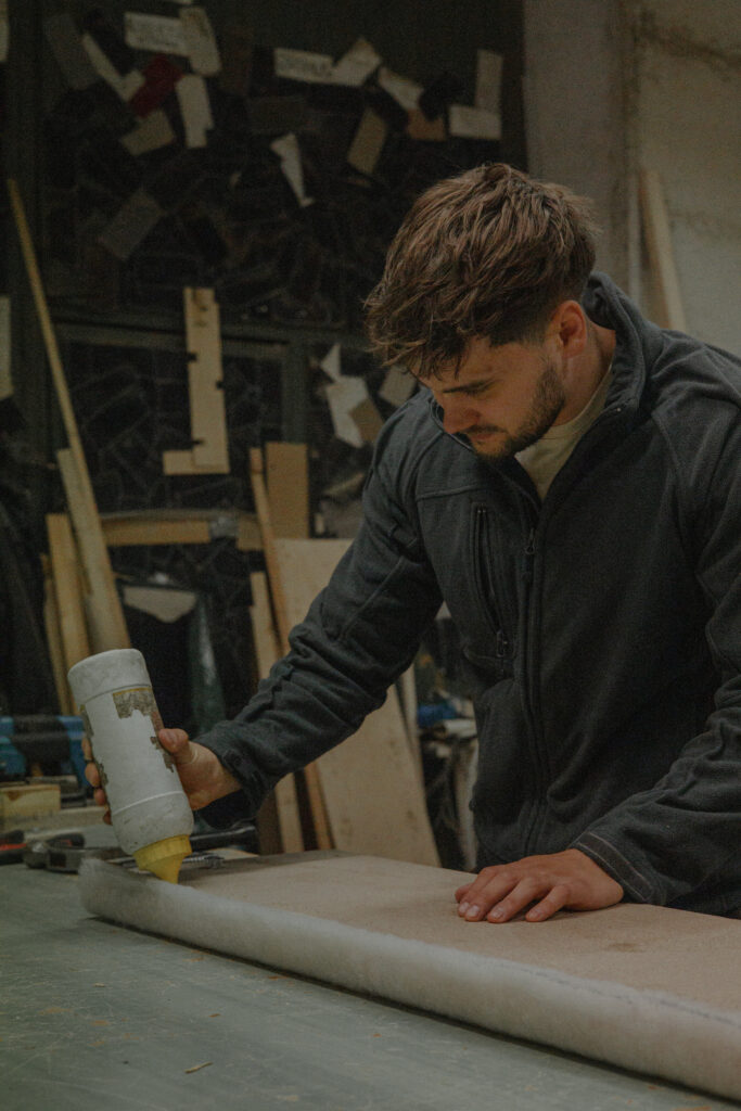 Työntekijä valmistelee huonekalun verhoilua levittämällä liimaa pintaan.